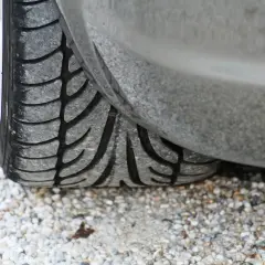 Gros plan sur un pneu de voiture usé, posé sur des graviers. Son usure pourrait être la cause d'un pneu bruyant.