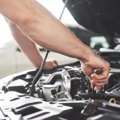 Un mécanicien effectue l'entretien de la voiture, serrant une pièce du moteur avec une clé.