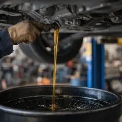 Vidange d'huile moteur d'un véhicule diesel, probablement à 30 000 km. L'huile usagée s'écoule dans un bac de récupération.