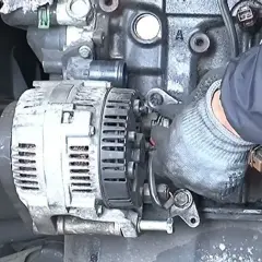 Main d'un mécanicien en gant travaillant sur un alternateur de voiture, étape clé pour apprendre comment changer un alternateur.