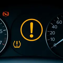 Tableau de bord avec voyant moteur point d'exclamation allumé, signalant un problème. Le témoin de pression des pneus est aussi actif.