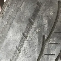 Gros plan sur un pneu de voiture montrant des pneus usés sur les bords, avec des craquelures visibles sur la bande de roulement.