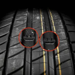 Gros plan sur la bande de roulement d'un pneu, avec deux indicateurs d'usure mis en évidence par des cercles rouges. Ces témoins sont cruciaux pour évaluer la durée de vie d'un pneu.