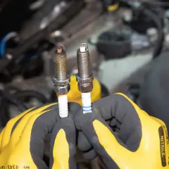 Gants jaunes tenant deux bougies d'allumage essence, l'une usée, l'autre neuve. Il est temps de savoir quand changer les bougies d'allumage essence.