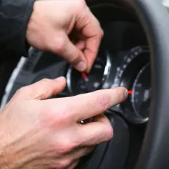 Main d'un mécanicien manipulant le tableau de bord, une astuce pour enlever le voyant airbag.