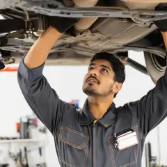 Mécanicien travaillant sous une voiture, inspectant le système d'échappement. Il pourrait être en train de vérifier comment nettoyer un catalyseur.