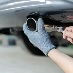 Main tenant, ganté, répare le pot d'échappement d'une voiture. Rouler sans pot d'échappement est bruyant et polluant.
