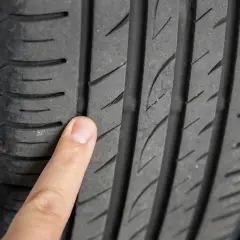 Un doigt pointe un pneu craquelé, montrant l'usure et les fissures sur la bande de roulement.