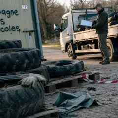 Un homme près d'un camion chargé de pneus agricoles. Un panneau indique "Campagne Pneus agricoles", un lieu où jeter des pneus usagés.