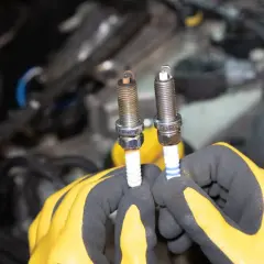Mains gantées tenant deux bougies d'allumage, une ancienne et une neuve, prêtes à changer.