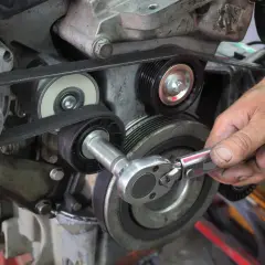 Main d'un mécanicien ajustant la tension courroie accessoire d'un moteur avec une clé à cliquet.