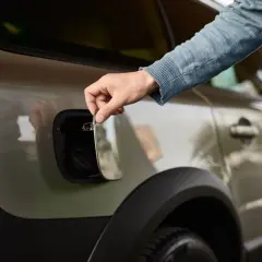 Main tenant ouvre la trappe à essence de sa voiture. Il soupire, pensant : "ma voiture consomme trop d'essence".