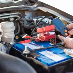 Main d'une personne utilisant un appareil pour tester une batterie de voiture qui se décharge. Les pinces rouges sont connectées à la batterie.