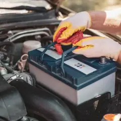 Mains gantées manipulent une batterie de voiture, peut-être pour résoudre un problème de batterie voiture.