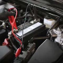 Main d'une personne portant un gant noir connectant des câbles de démarrage à la batterie d'une voiture qui s'éteint en roulant.