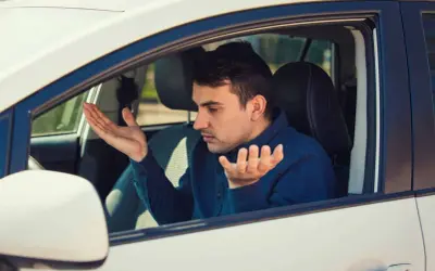 Homme frustré dans sa voiture qui tremble au point mort, mains levées en signe d'incompréhension.