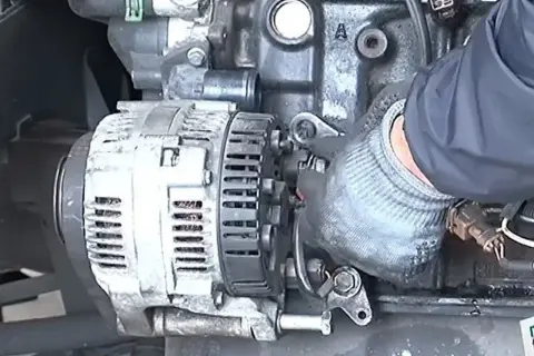 Main d'un mécanicien en gant travaillant sur un alternateur de voiture, étape clé pour apprendre comment changer un alternateur.