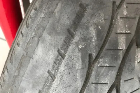 Gros plan sur un pneu de voiture montrant des pneus usés sur les bords, avec des craquelures visibles sur la bande de roulement.