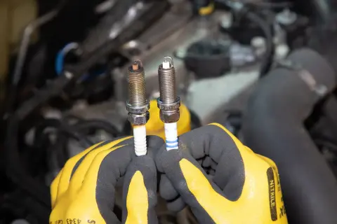 Gants jaunes tenant deux bougies d'allumage essence, l'une usée, l'autre neuve. Il est temps de savoir quand changer les bougies d'allumage essence.