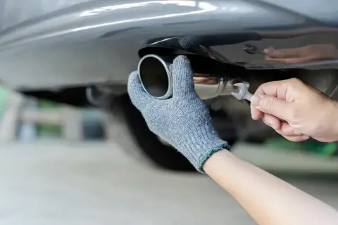 Main tenant, ganté, répare le pot d'échappement d'une voiture. Rouler sans pot d'échappement est bruyant et polluant.