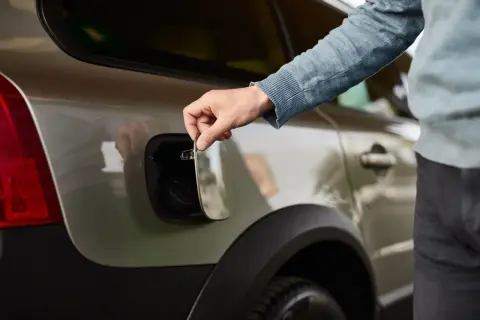 Main tenant ouvre la trappe à essence de sa voiture. Il soupire, pensant : "ma voiture consomme trop d'essence".