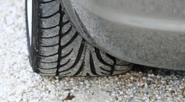 Gros plan sur un pneu de voiture usé, posé sur des graviers. Son usure pourrait être la cause d'un pneu bruyant.