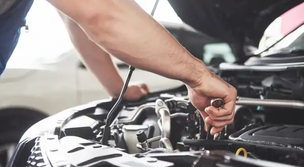 Un mécanicien effectue l'entretien de la voiture, serrant une pièce du moteur avec une clé.
