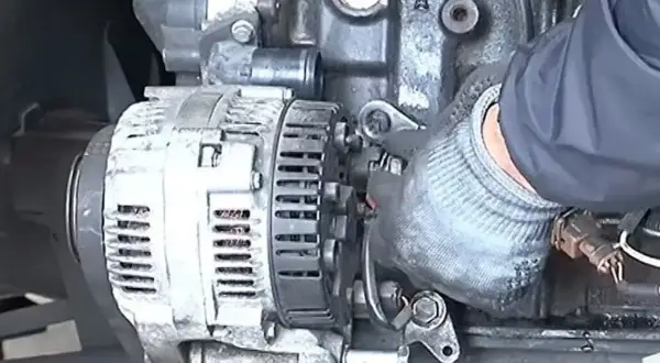 Main d'un mécanicien en gant travaillant sur un alternateur de voiture, étape clé pour apprendre comment changer un alternateur.