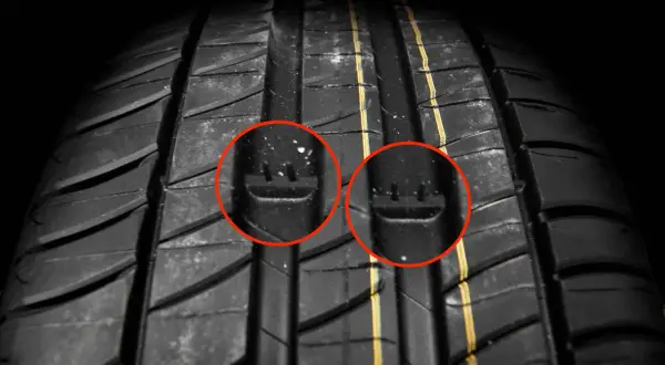 Gros plan sur la bande de roulement d'un pneu, avec deux indicateurs d'usure mis en évidence par des cercles rouges. Ces témoins sont cruciaux pour évaluer la durée de vie d'un pneu.