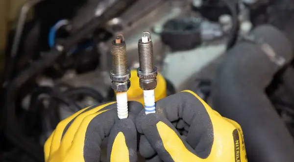 Gants jaunes tenant deux bougies d'allumage essence, l'une usée, l'autre neuve. Il est temps de savoir quand changer les bougies d'allumage essence.
