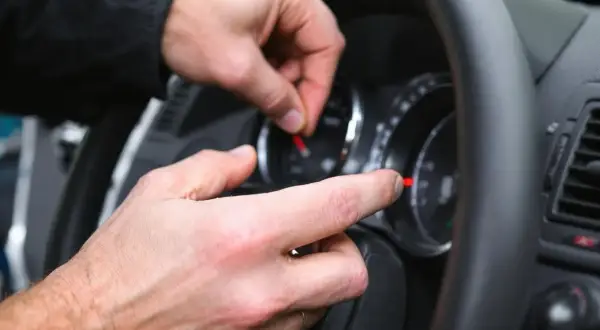 Main d'un mécanicien manipulant le tableau de bord, une astuce pour enlever le voyant airbag.