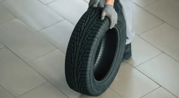 Mains gantées tenant un pneu, le motif de la bande de roulement indique le sens de rotation pneu sans flèche.