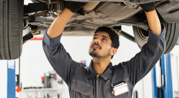 Mécanicien travaillant sous une voiture, inspectant le système d'échappement. Il pourrait être en train de vérifier comment nettoyer un catalyseur.