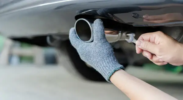 Main tenant, ganté, répare le pot d'échappement d'une voiture. Rouler sans pot d'échappement est bruyant et polluant.
