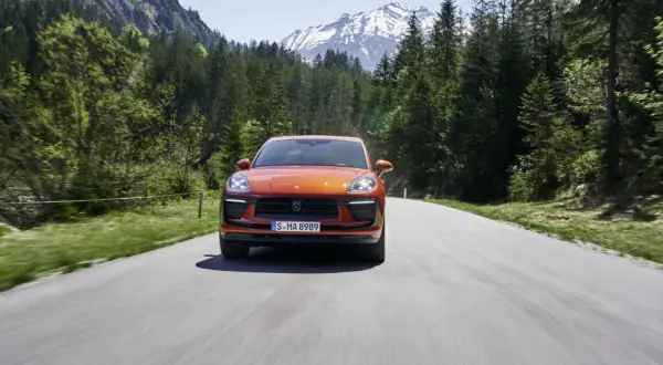 Porsche Macan orange sur une route de montagne, respectant la norme européenne d'émissions.