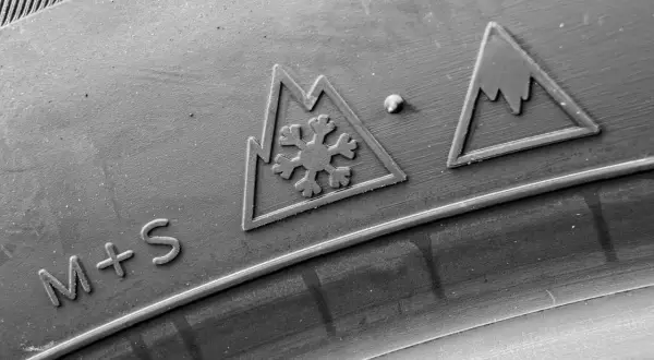 Gros plan sur un pneu avec les marquages "M+S" et le symbole 3PMSF (flocon dans une montagne), indiquant sa capacité à affronter la neige.