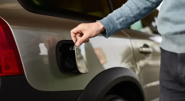 Main tenant ouvre la trappe à essence de sa voiture. Il soupire, pensant : "ma voiture consomme trop d'essence".