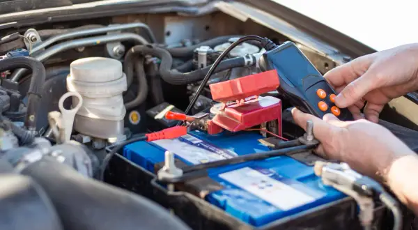 Main d'une personne utilisant un appareil pour tester une batterie de voiture qui se décharge. Les pinces rouges sont connectées à la batterie.