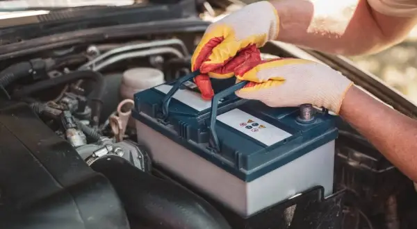 Mains gantées manipulent une batterie de voiture, peut-être pour résoudre un problème de batterie voiture.