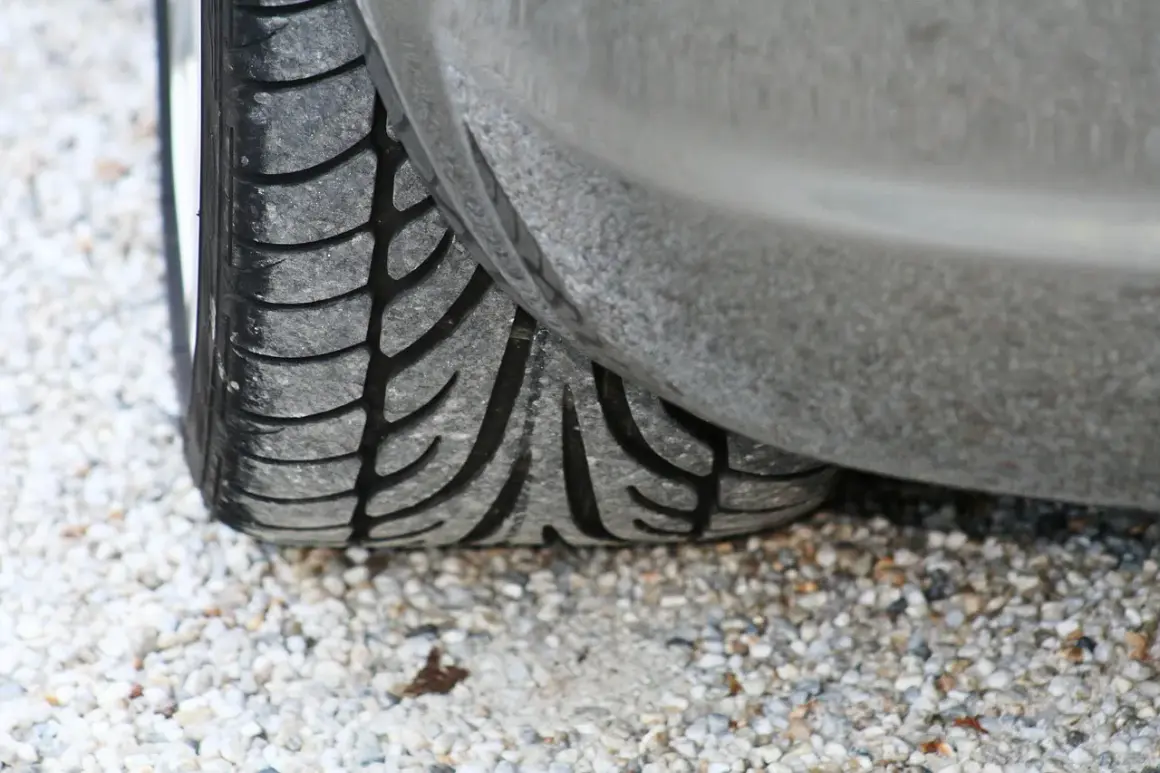 Gros plan sur un pneu de voiture usé, posé sur des graviers. Son usure pourrait être la cause d'un pneu bruyant.