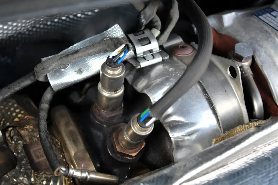 Deux sondes lambda rouillées, un symptôme de sonde lambda défectueuse, sont visibles sous un blindage thermique.