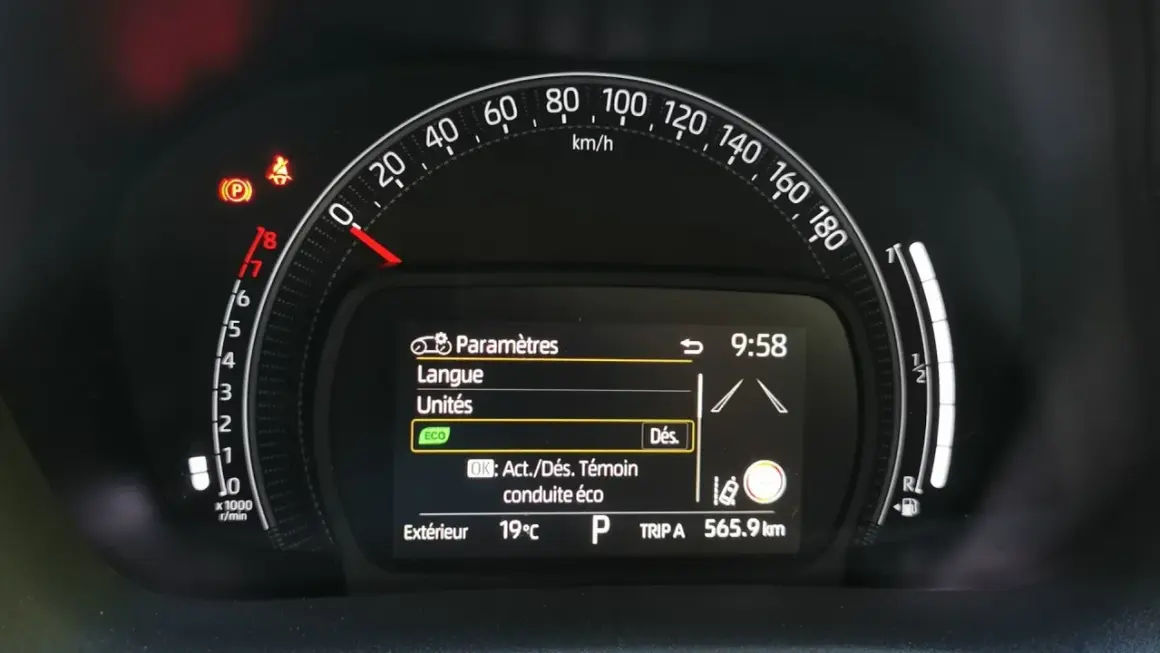Tableau de bord Toyota Aygo X : voyant pression pneu allumé, menu paramètres affiché. Vitesse 0 km/h, température extérieure 19°C.