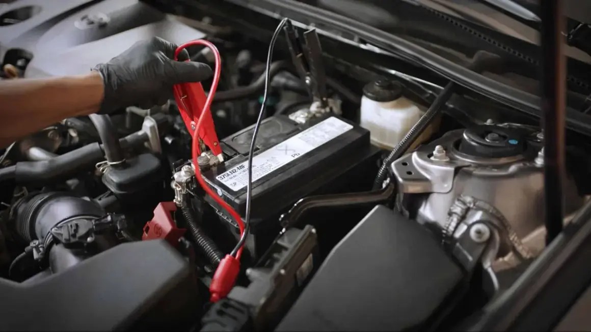Main d'une personne portant un gant noir connectant des câbles de démarrage à la batterie d'une voiture qui s'éteint en roulant.