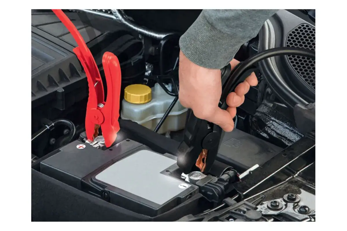 Main d'une personne connectant des c&acirc;bles pour d&eacute;marrer une voiture, qu'elle soit &agrave; essence ou diesel.