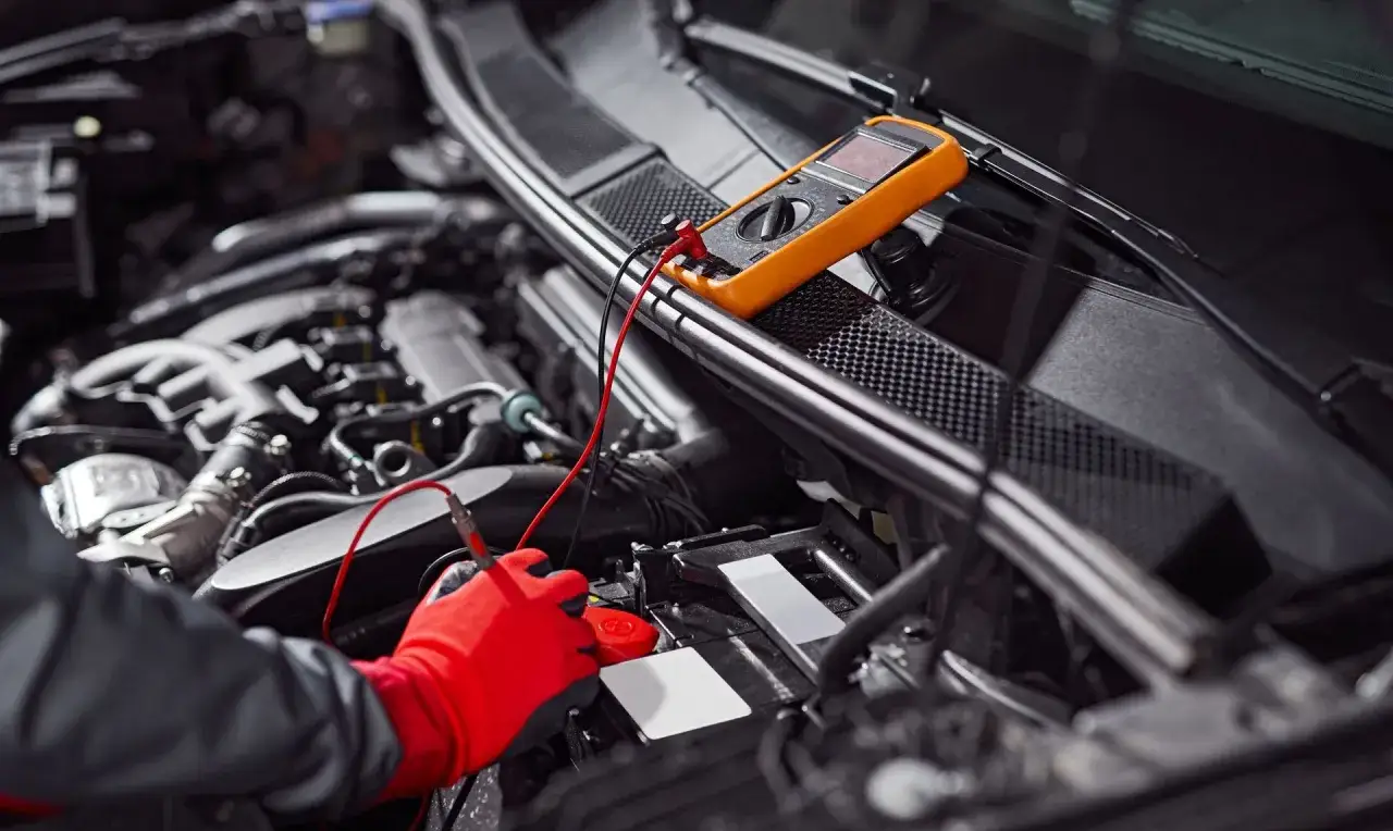 Un m&eacute;canicien v&eacute;rifie une batterie qui chauffe avec un multim&egrave;tre. Les c&acirc;bles rouges et noirs sont connect&eacute;s &agrave; la batterie.