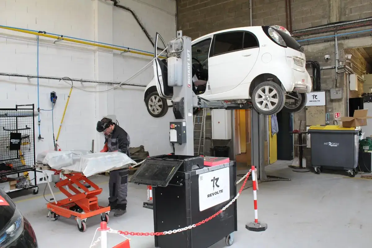 Un m&eacute;canicien pr&eacute;pare la vidange d'une voiture &eacute;lectrique sur un pont &eacute;l&eacute;vateur dans un atelier.