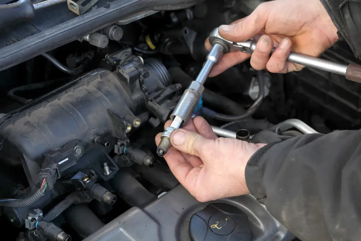 Mains d'un m&eacute;canicien utilisant une cl&eacute; pour changer une bougie d'allumage sur un moteur de voiture.
