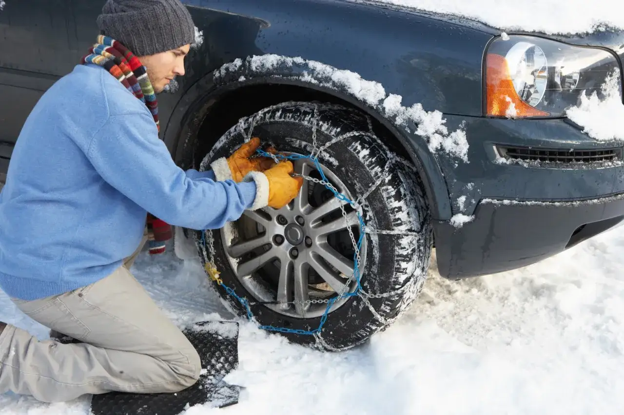 Un homme met des cha&icirc;nes sur les pneus de sa voiture dans la neige. Il faut bien mettre chaussettes pneus pour rouler en s&eacute;curit&eacute;.