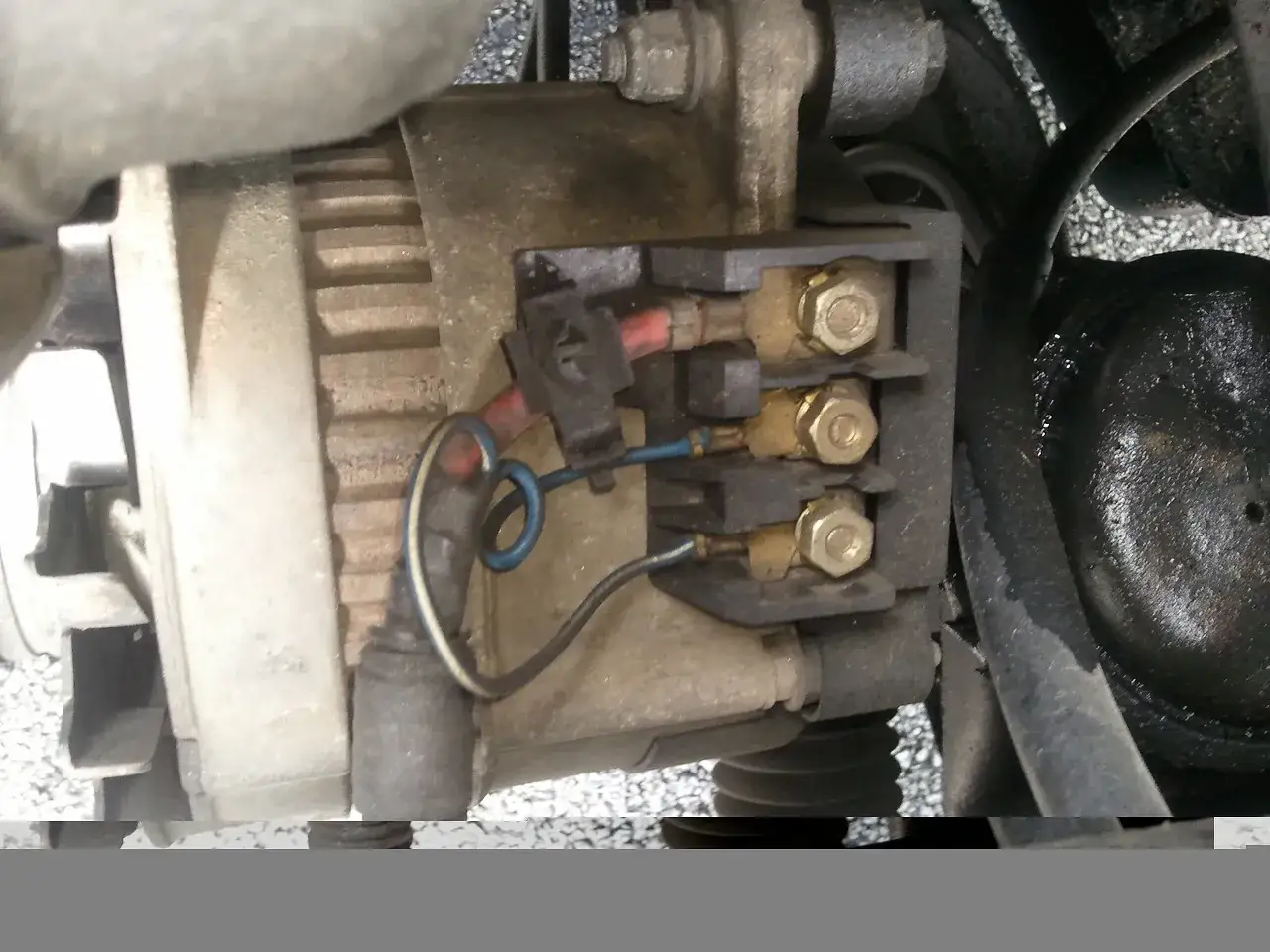 Connexion du r&eacute;gulateur d'alternateur avec ses fils rouges et bleus, fix&eacute;s par des boulons dor&eacute;s sur un support noir.