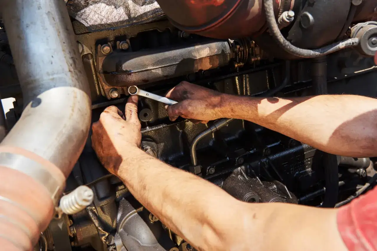 M&eacute;canicien travaillant sur un moteur diesel, peut-&ecirc;tre pour r&eacute;soudre un sympt&ocirc;me injecteur encrass&eacute;. Mains sales utilisant une cl&eacute;.